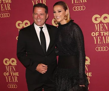 Man and woman posing at GQ Men of the Year event, wearing formal attire, smiling in front of a branded backdrop.