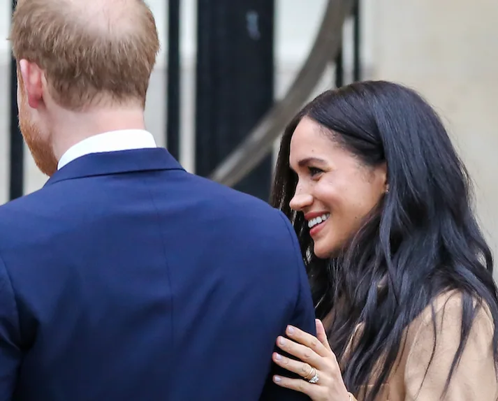 Smiling woman with dark hair holds a man in a blue suit outside.