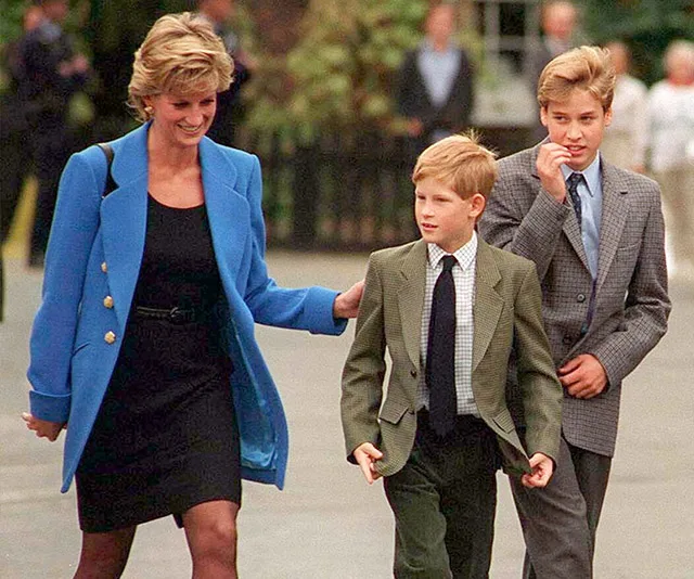 Princess Diana walking with her two young sons, both dressed in suits, outdoors.