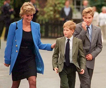 Princess Diana walking with her two young sons, both dressed in suits, outdoors.