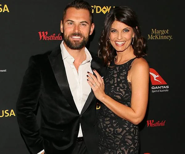 A couple poses on the red carpet in formal attire at an event, smiling at the camera.