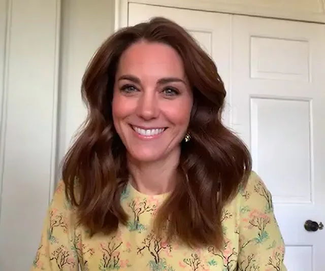 Woman smiling in yellow patterned top, sitting indoors with a closed door in the background.