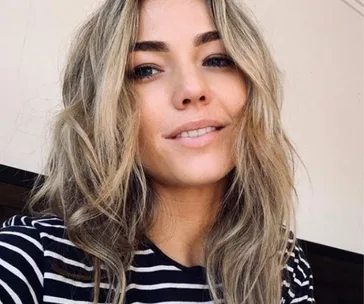 Young woman with wavy blonde hair and a striped shirt, smiling softly at the camera.
