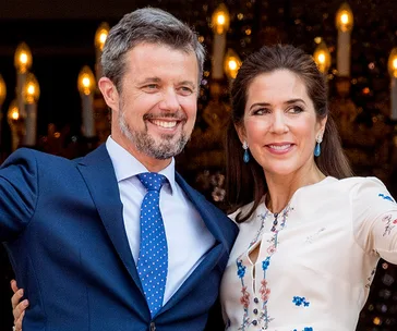 Crown Prince Frederik and Crown Princess Mary smiling at a formal event with lit chandeliers in the background.