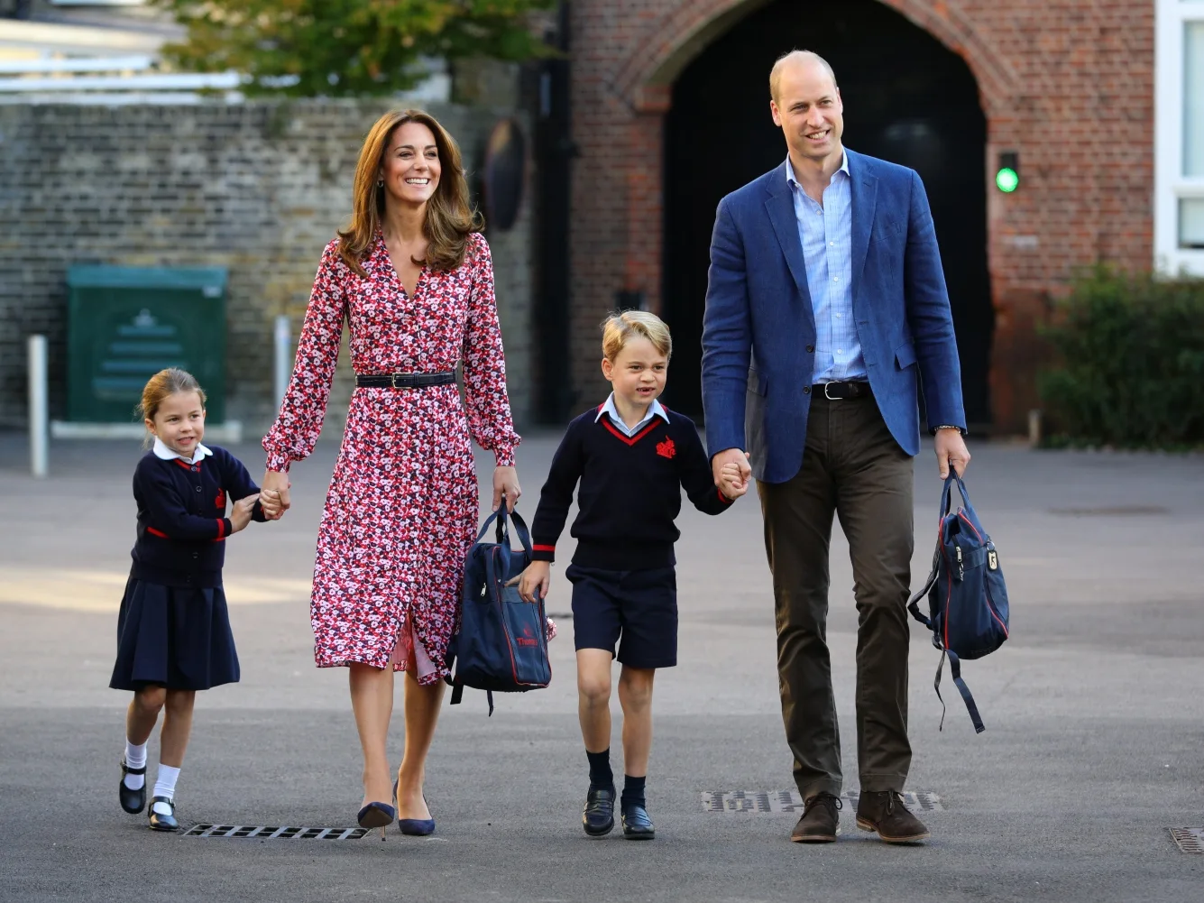 A family with two children in school uniforms walking happily together, carrying backpacks.