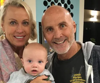 Grandparents smiling and holding their young grandchild indoors.