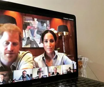"Video call on laptop screen with two people in a well-lit room, surrounded by framed art and lamps in background."