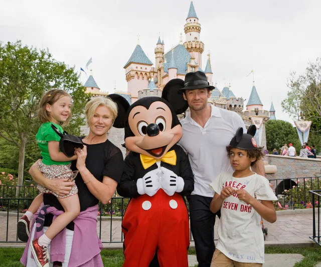 Family with Mickey Mouse in front of a Disney castle, enjoying a theme park visit.