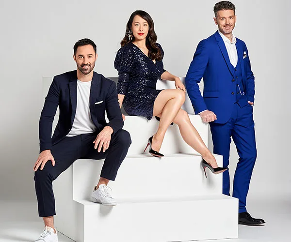 Three people in formal attire posing confidently on white steps against a plain background.