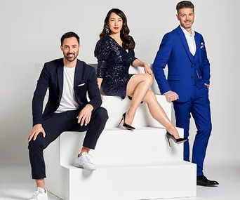Three people in formal attire posing confidently on white steps against a plain background.