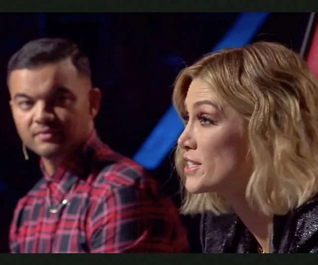 Two people are sitting side by side; one is speaking, and the other is looking attentively at them.