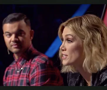 Two people are sitting side by side; one is speaking, and the other is looking attentively at them.