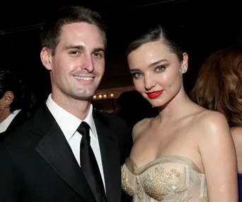 A couple dressed elegantly, with the woman in a strapless dress and the man in a suit, smiling at a formal event.