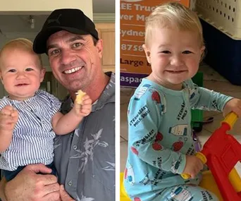 Man in a cap holding a smiling baby, and another baby in pajamas sitting and smiling joyfully.