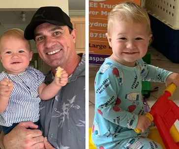 Man in a cap holding a smiling baby, and another baby in pajamas sitting and smiling joyfully.