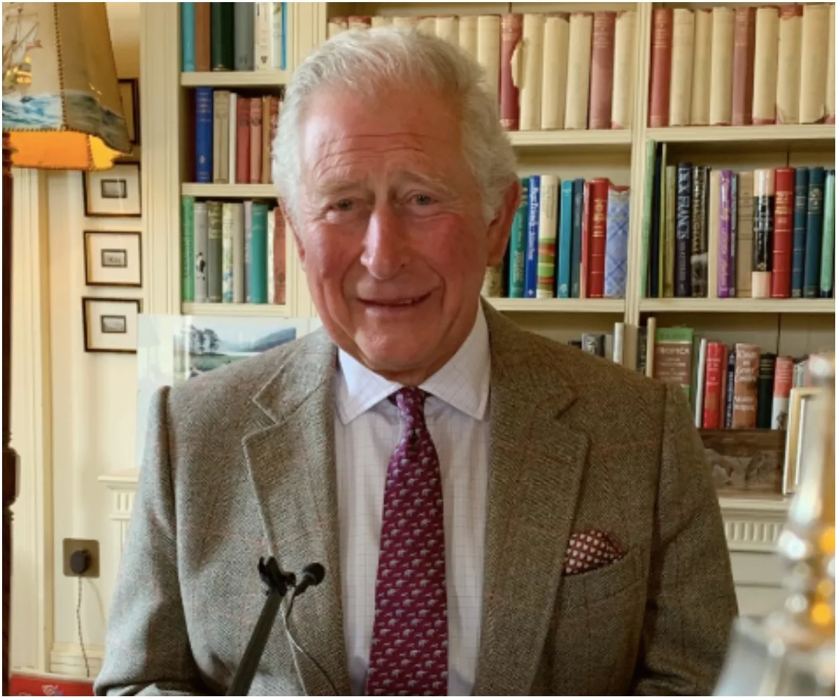 A person in a suit and tie stands in front of bookshelves, smiling, in a well-lit room.