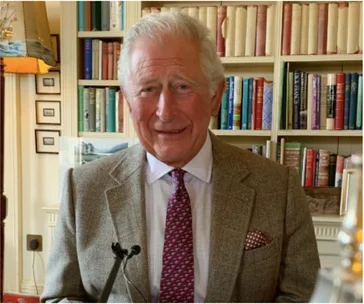 A person in a suit and tie stands in front of bookshelves, smiling, in a well-lit room.