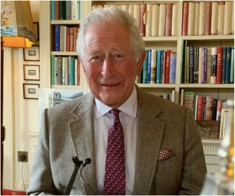 A person in a suit and tie stands in front of bookshelves, smiling, in a well-lit room.