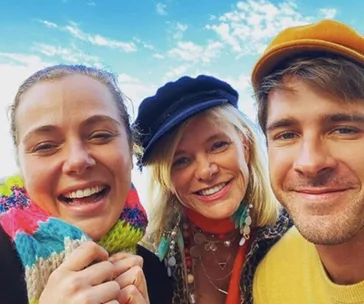 Three people smiling for a selfie under a clear sky, wearing colorful clothing and hats.