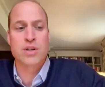 A person speaking on a video call, seated in a room with bookshelves.