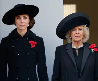 Two women in black coats and hats with poppy pins, standing solemnly.
