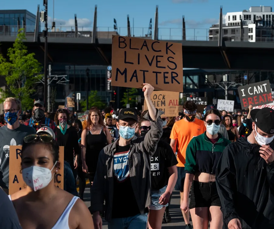 Protesters wearing masks hold "Black Lives Matter" signs during a daytime demonstration.