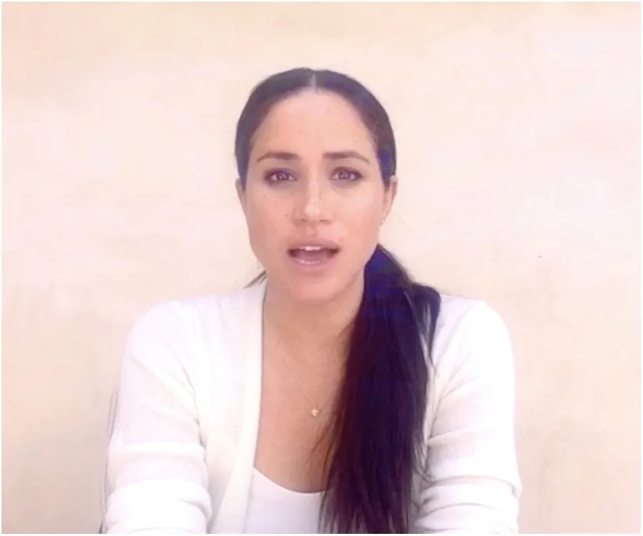 A woman with long dark hair speaking in a white top against a plain background.