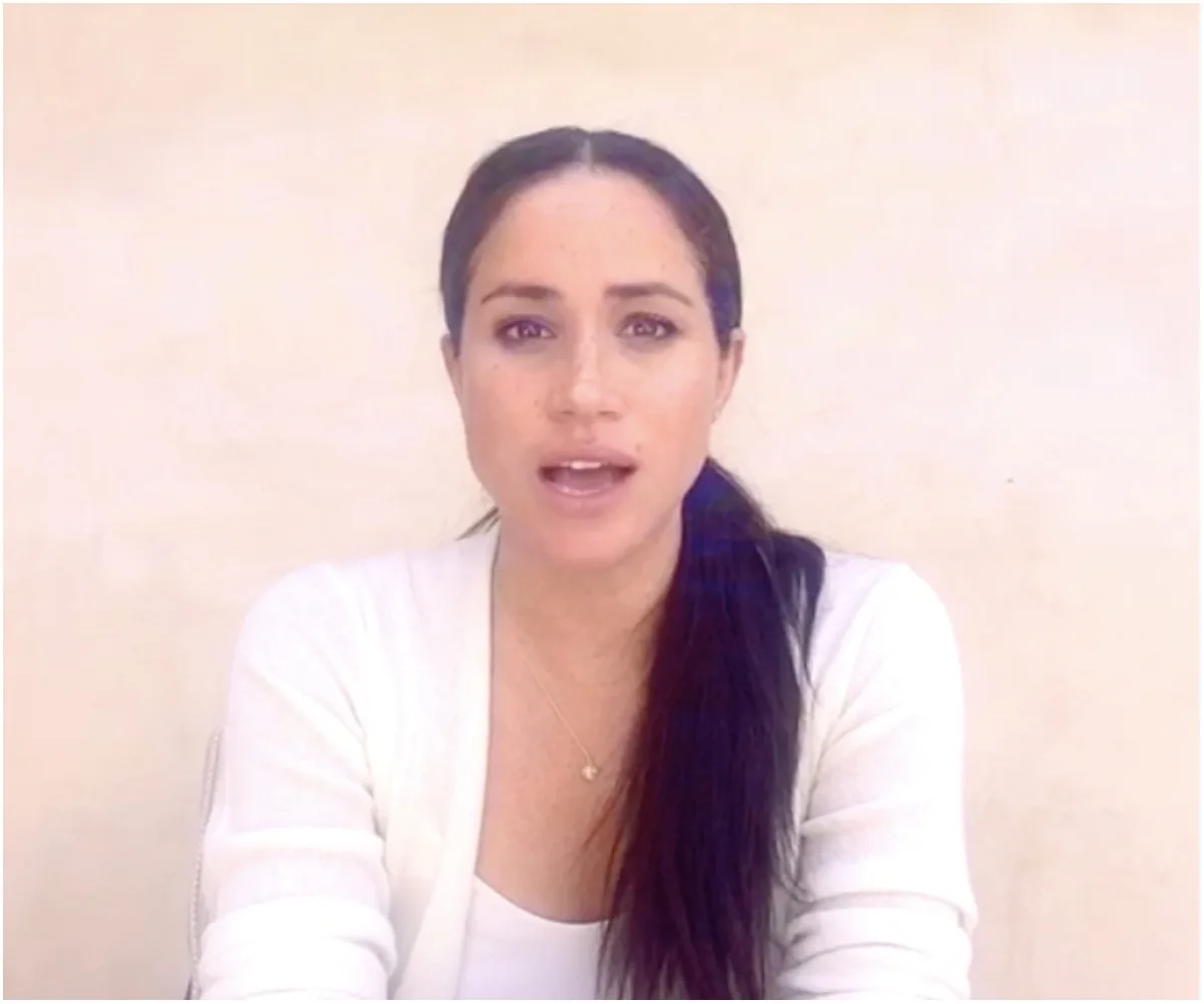 A woman with long dark hair speaking in a white top against a plain background.