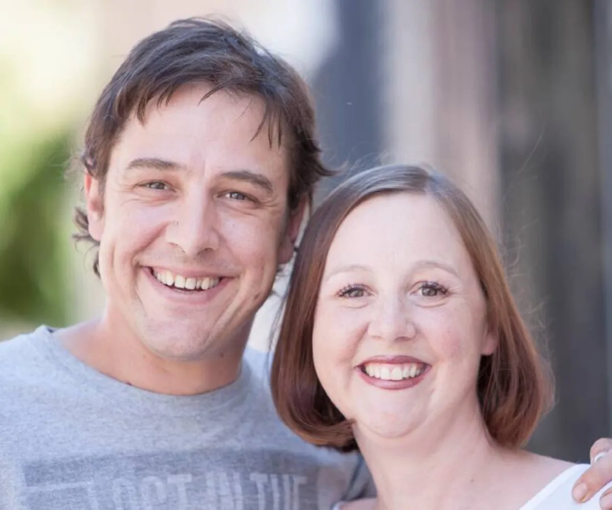 Two people, a man and a woman, smiling warmly while posing closely for a photo outdoors.