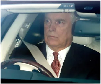 Man in a car wearing a suit and red tie, looking ahead through the windshield.