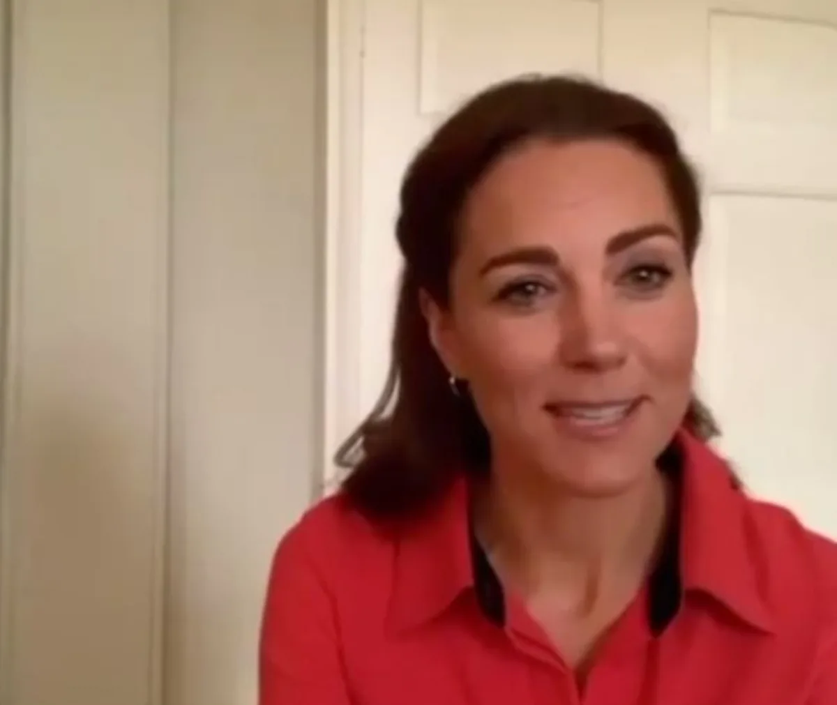 A person wearing a red blouse, smiling during a virtual meeting in front of a white door.