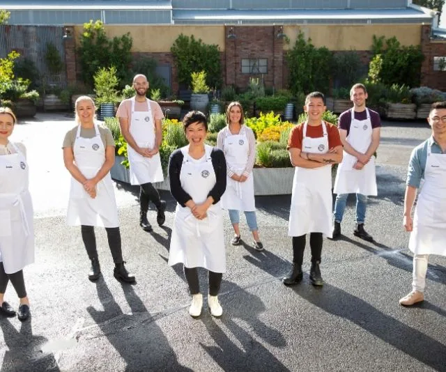 Eight MasterChef 2020 contestants wearing aprons, standing outdoors in a garden setting, smiling for the camera.