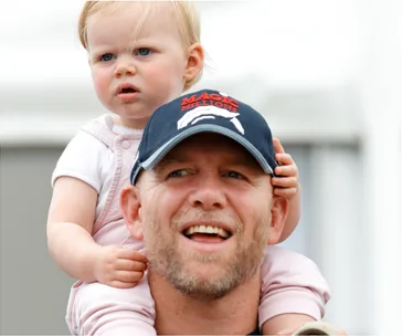Man wearing a cap with a child on his shoulders, smiling outdoors.