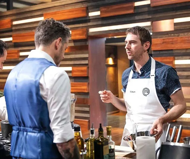 Two contestants on MasterChef Australia converse in the kitchen, one wearing a white apron with "Callum" on it.