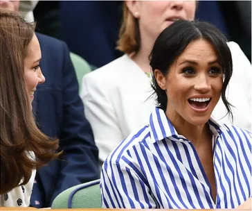 Two women smiling and talking, one in a striped shirt, seated in a crowded event.