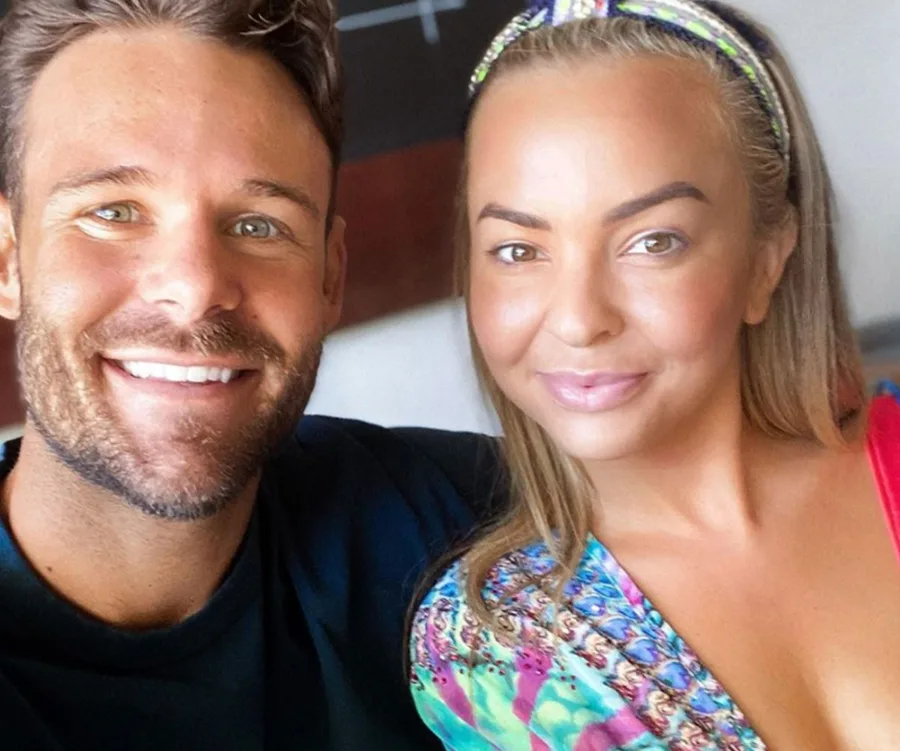 Two people smiling closely together, one wearing a patterned top.