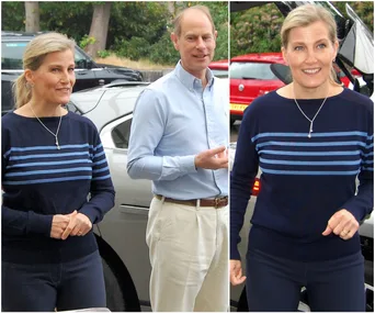 Two people outside, one wearing a striped sweater and jeans, standing near a car with trees in the background.