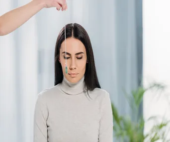 Person undergoing hypnosis session, with eyes closed and a pendant swinging in front of them.