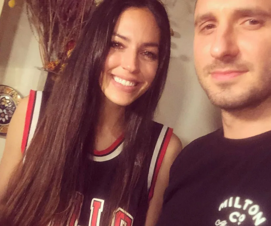 A man and woman smiling in a casual indoor setting, with a basketball jersey and decorative background.