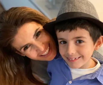 A woman and a boy, both smiling at the camera; the boy is wearing a stylish grey hat and blue shirt.