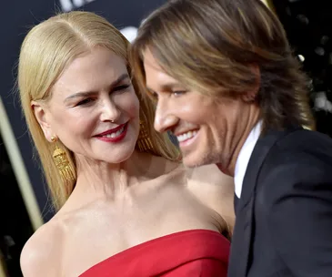 Nicole Kidman in a red dress smiles at an event, standing beside Keith Urban in a suit.