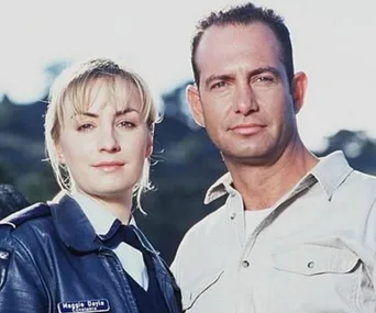 Maggie Doyle and a male character from "Blue Heelers" TV show standing outdoors, both looking at the camera.