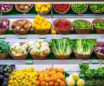 Baskets of fresh organic produce like peppers, citrus fruits, and greens displayed on grocery shelves.
