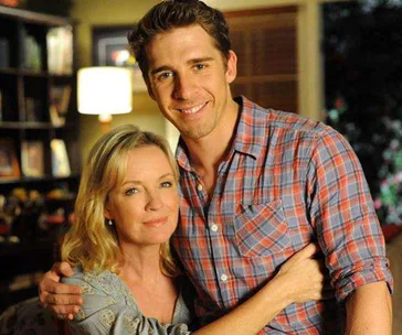 A woman and a man smiling and hugging in a warmly lit room with a bookshelf in the background.