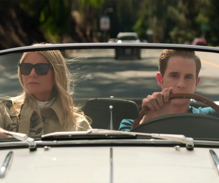 Two people in sunglasses driving a convertible on a sunny road.