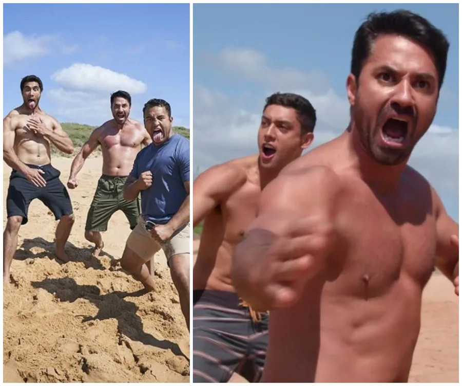Three men perform a haka on a sandy beach, showing intense expressions and athletic poses under a clear sky.