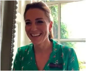 "Smiling woman in green tennis-themed blouse near a window."