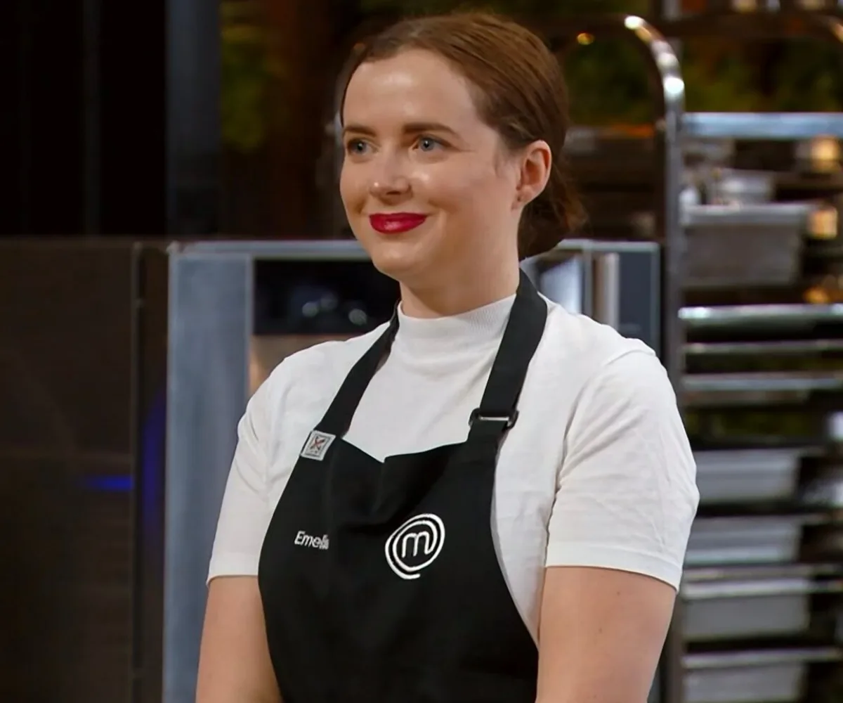 Emelia Jackson wearing a black MasterChef apron, smiling in a kitchen setting.