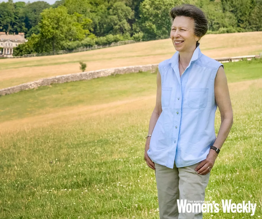 A woman in a sleeveless blouse smiles at a scenic countryside landscape.