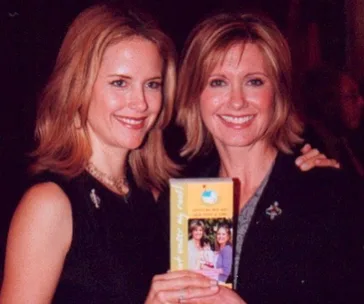 Two women smiling, one holding a book featuring both on the cover.